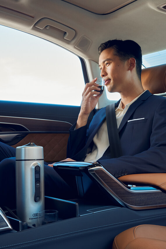 a man in the back seat sipping coffee made from an Audi mobile expresso machine