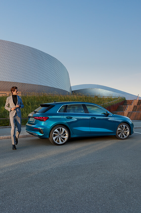 side view of Audi A3 Sportback parked outside a modern building with a man standing at the rear