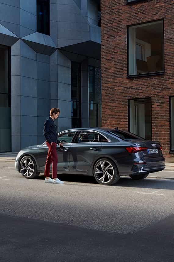 side view of Audi A3 Sedan parked outside a modern building with a man standing at the rear