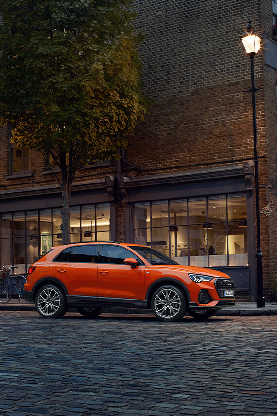 side view of Audi Q3 parked on a brick road outside a building with glass windows